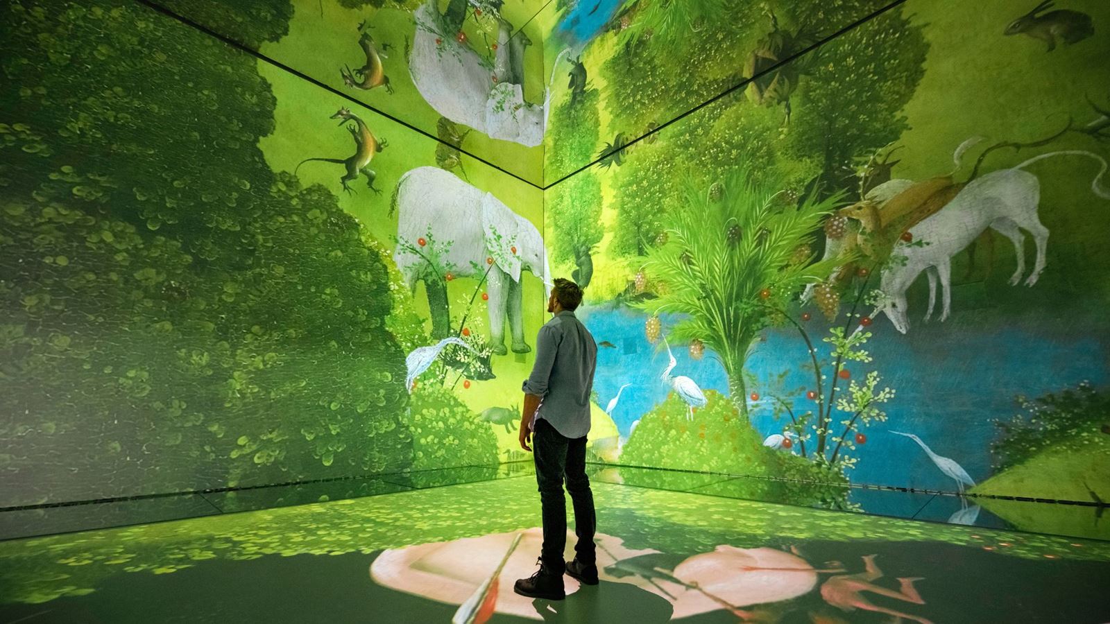 A man stands in front of an immersive artwork piece with a green garden and animals at frameless london.