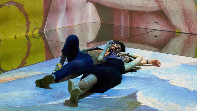 Two people laying on floor surrounded by immersive art on walls and floor.