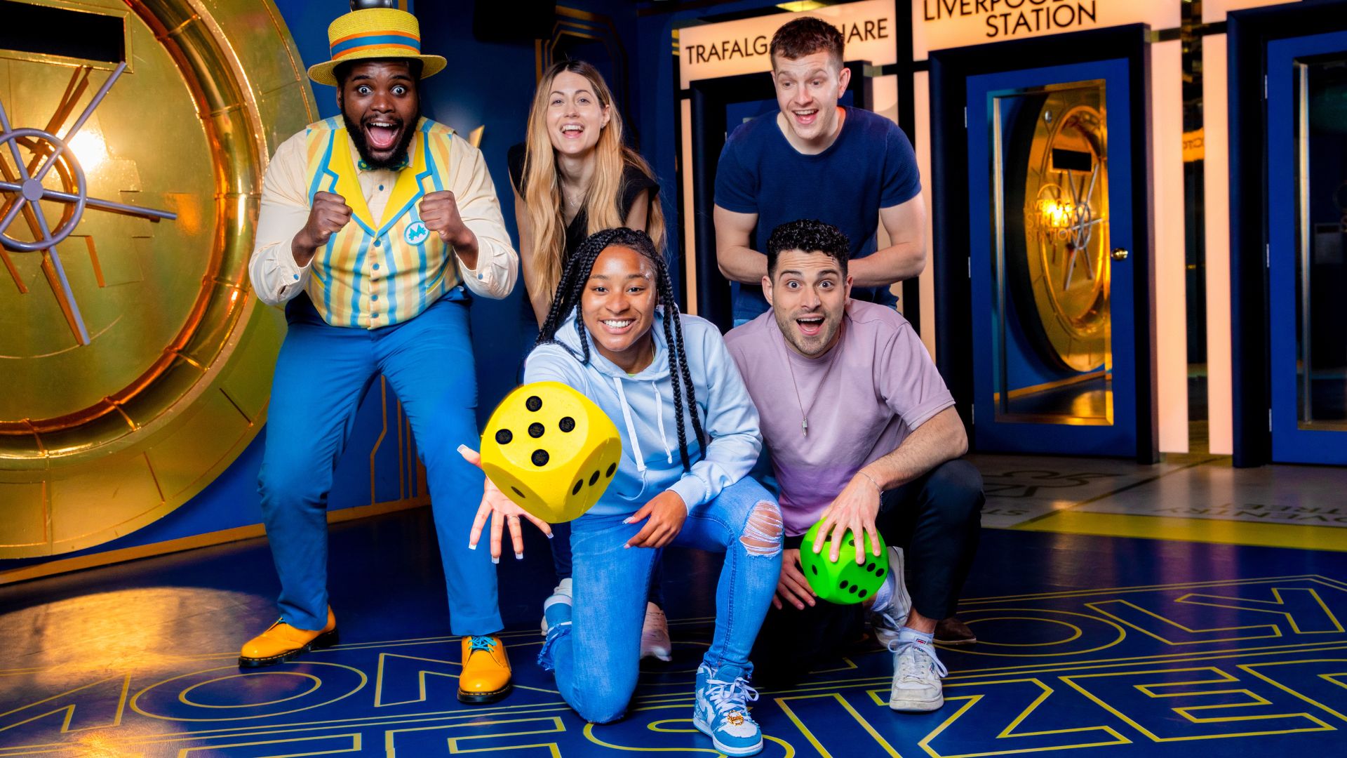 Complete escape room-style challenges and compete to win at Monopoly Lifesized. Image courtesy of Monopoly Lifesized. five adults crouching down ready to throw a dice in an immersive experience game room