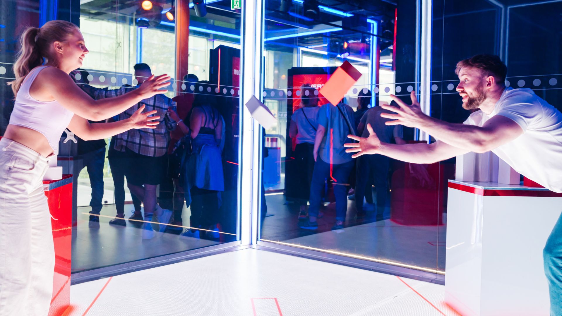 Play iconic immersive games from the original BAFTA-winning TV series. Image courtesy of Carver PR. large glass cube box with two people playing an interactive game throwing foam blocks to eachother