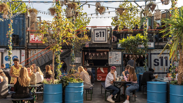 People sat outside on benches at Pop Brixton market surrounded by greenery