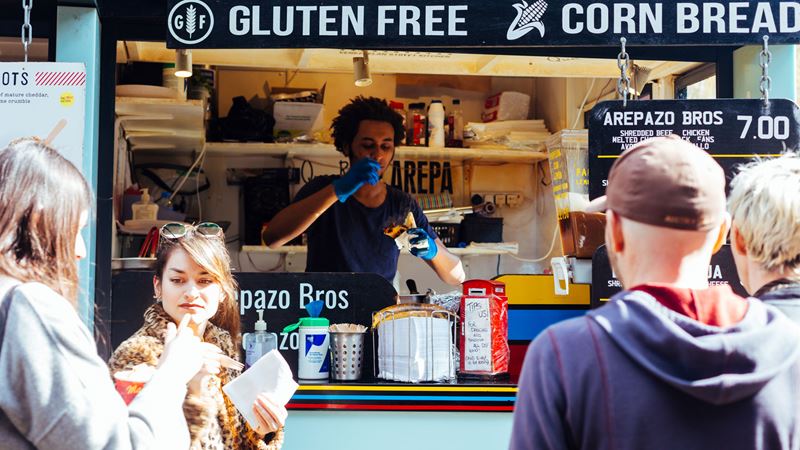 Stroll around Camden Market tasting foodie delights from across the globe. Credit: Shutterstock. Image courtesy of Shutterstock. People enjoying food from a food stall in Camden
