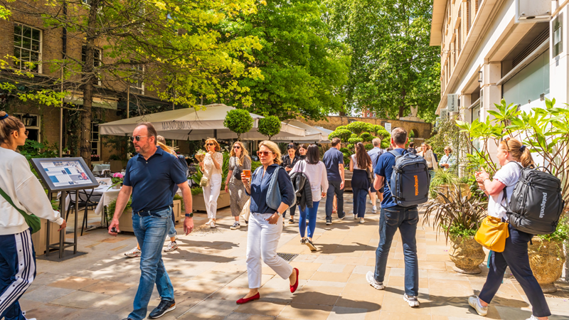 A trip to Chelsea is not complete without a visit to Duke of York Square. Credit: Shutterstock. Image courtesy of Shutterstock. People dressed up in smart/casual clothes walking around Duke of York Square on a sunny day with bright green trees in the background and outside restaurant seating