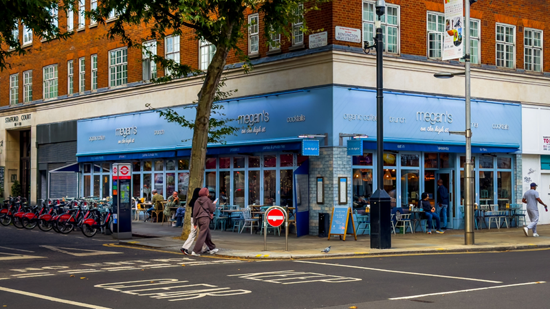 Treat yourself to a mouthwatering brunch at Megan's Cafe in Chelsea. Credit: Shutterstock. Image courtesy of Shutterstock. A photo of Megan's Cafe in Chelsea from outside, a light blue building on a corner with people walking outside and a Santander docking station