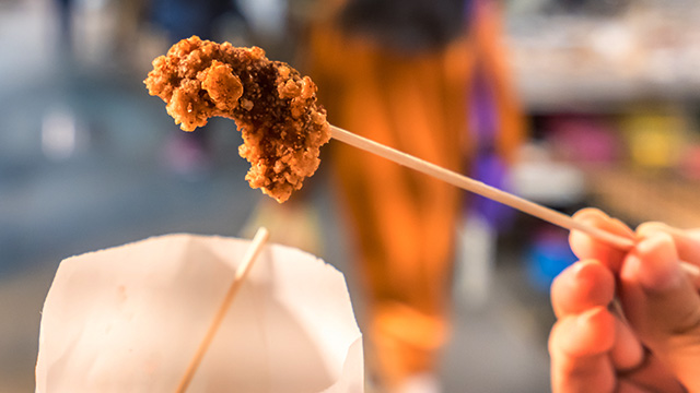 Fried chicken is the specialty at Good Friend. Image courtesy of Shutterstock. Hand holding a skewer of fried chicken at Good Friend in London Chinatown.