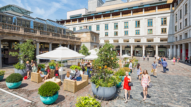 Visit Covent Garden © Brendan Bell / Photos.London. Image courtesy of Brendan Bell / Photos.London. People sitting in the square at Covent Garden with women strolling past in the sun