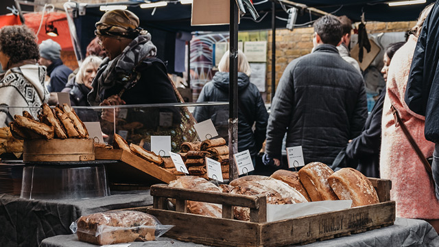 A row of shops interrupted by a curved sign reading 'Greenwich Market' hung above an alleyway.