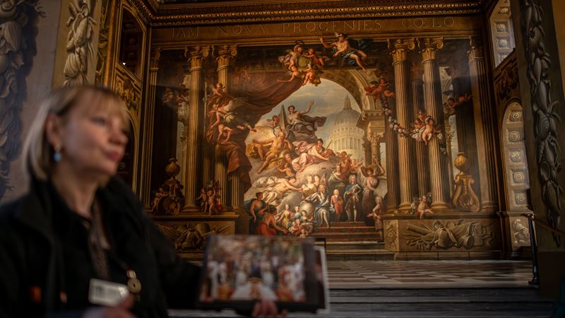 Enjoy a guided tour of the Painted Hall in Greenwich and find out more about what goes on behind the scenes at this iconic film location. ©London & Partners/Michael Barrow A tour guide shows a photo of a scene filmed inside the Painted Hall in Greenwich.