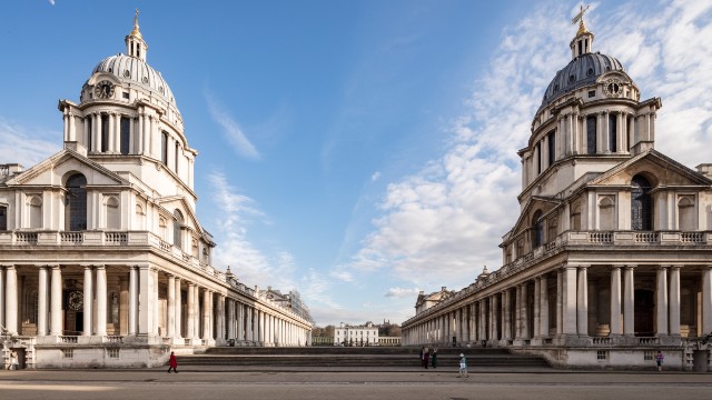 A historic white stone building with columns and two large domes on the roof.