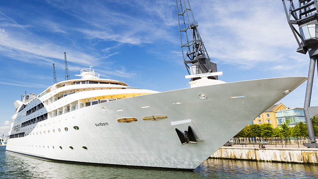Large white yacht anchored in a harbour with blue sky and white sweeping clouds behind.