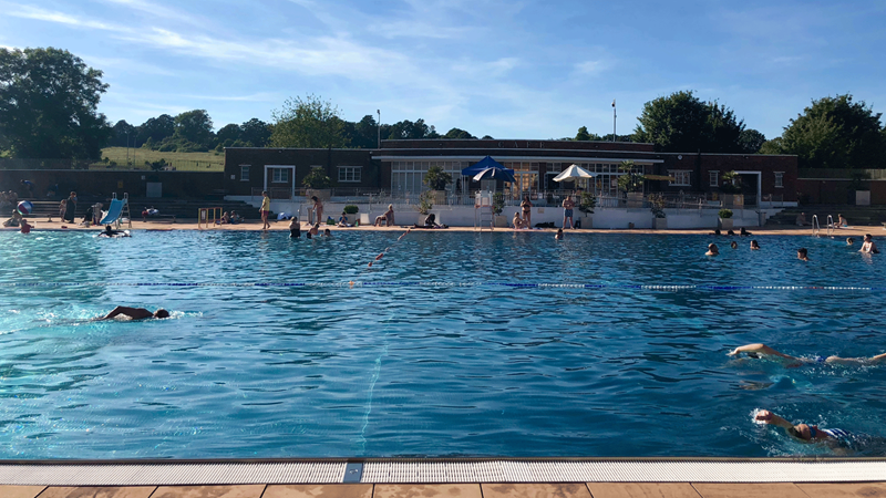 People swim in the lido at Hampstead Heath with a view of the park in the background