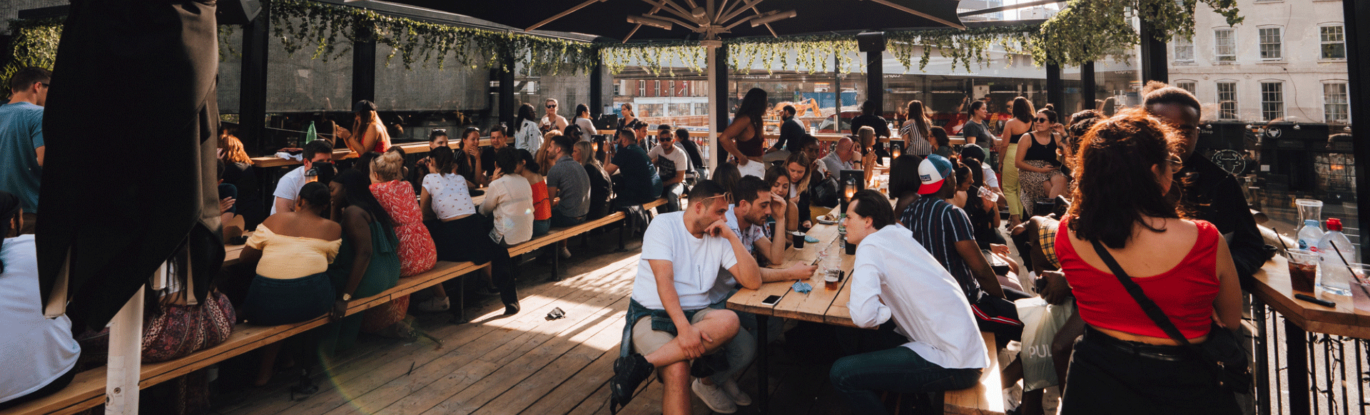 People sit on benches on the rooftop of Boxpark with bridge in the background