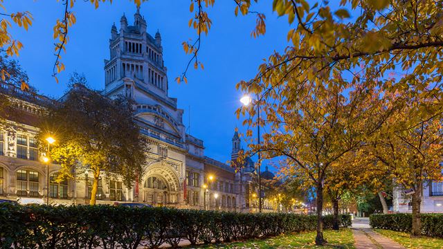 Victoria and Albert Museum facade at night, with trees in the foreground.