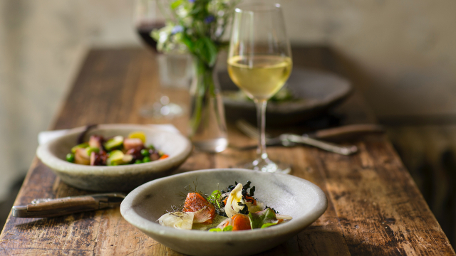 A close-up of two beautifully-dressed plates and a glass of white wine on a rustic wooden table.