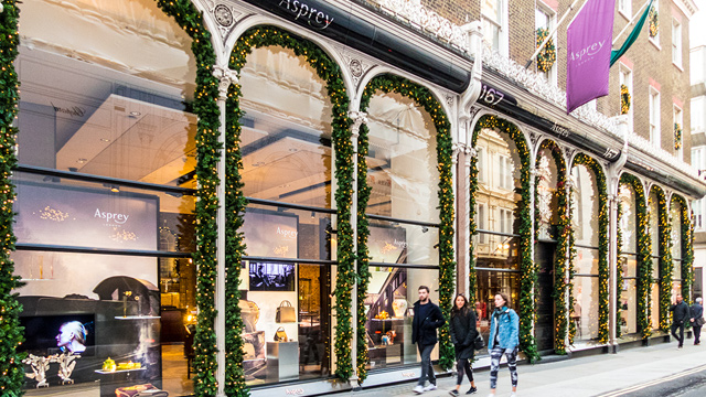 See shops adorned with festive lights on Bond Street in the run-up to Christmas. Image courtesy of Shutterstock. People walking past glass window shop fronts on Bond Street in London's Mayfair.