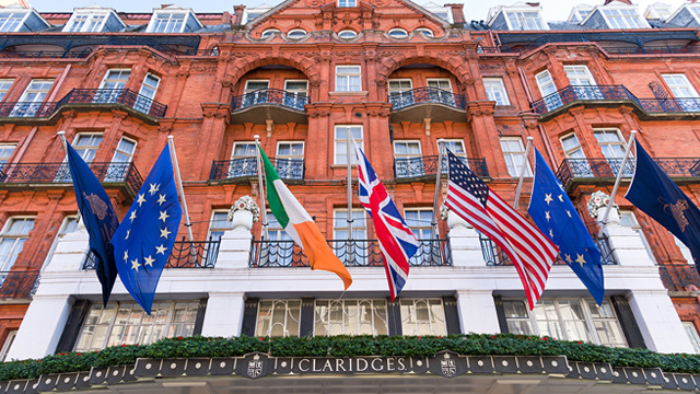 Stay at iconic Claridge's in Mayfair. Image courtesy of Shutterstock. Red-brick facade of Claridge's hotel in London's Mayfair, adorned with international flags.