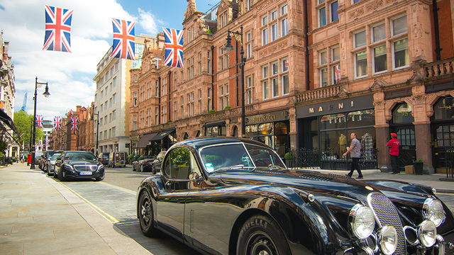 Explore stylish Mount Street, one of Mayfair's main shopping hubs. Image courtesy of Shutterstock. Expensive black cars parked on stylish Mount Street in London's Mayfair, with UK flags hanging between red-brick buildings in the background.