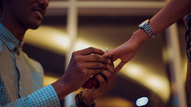 A man in a checked shirt putting a ring on a woman's finger.