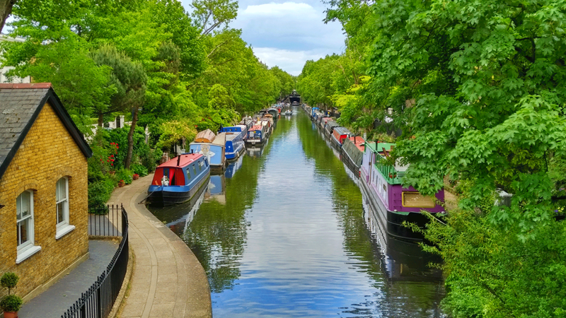 Meander around the scenic waterside location seen in the Paddington 2 movie. Credit: Shutterstock. Image courtesy of Shutterstock. Image of boats and river surrounded by leafy trees in Little Venice