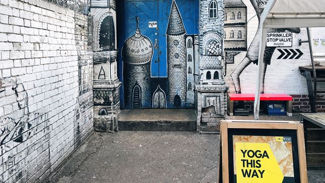 Street art of a castle on a blue door way behind a yellow sign reading Yoga this way