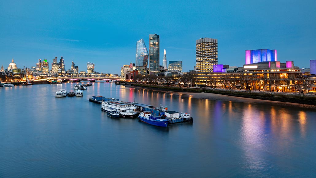 The river Thames at dusk, looking across to the South Bank and Bankside, with boats on the water.