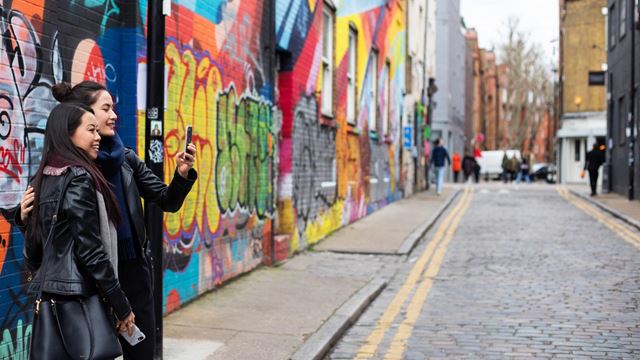 Two women take a selfie in front of colourful street art in a Shoreditch street.