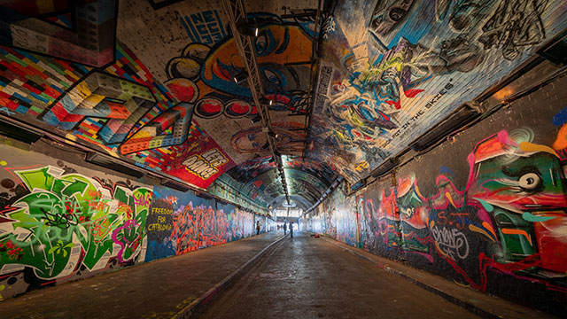 Looking along an empty Leake Street Tunnel, which is decorated with colourful street art on the walls and ceiling, with daylight visible at the end of the tunnel.