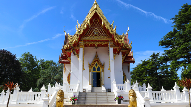Intricate white and gold details on the Buddhapadipa Temple surrounded by trees on a clear blue day