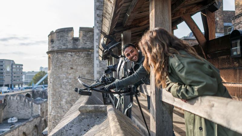 Stand on the battlements of the iconic Tower of London. Credit: London & Partners/Michael Barrow. Image courtesy of visitlondon.com. Two people stand on the stone battlements next to a crossbow on the tower of london.