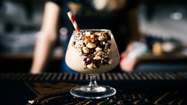 A large glass filled with a chocolate cocktail and a stripey red and white straw. 
