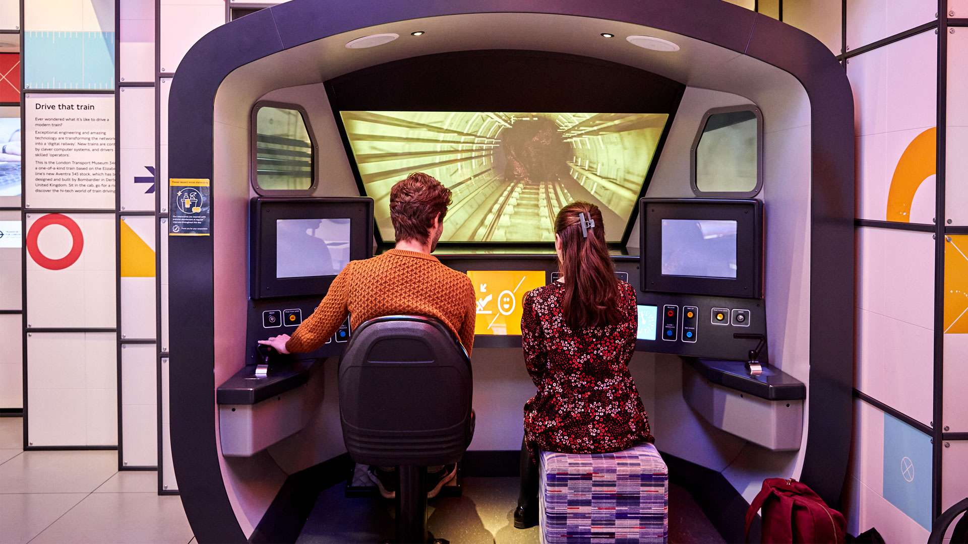 two people sat at a Tube driving simulator
