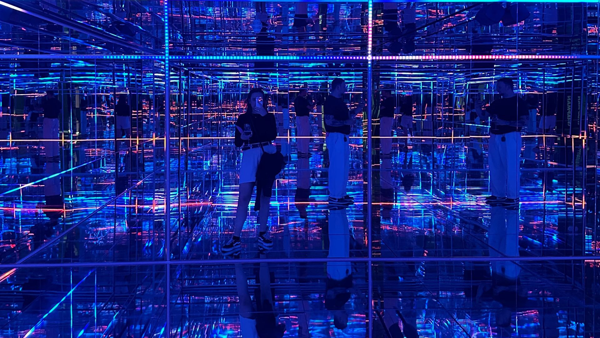 Be immersed in Pulse Interactive by Daan van Hasselt at Moco Museum. © Visit London/Kirstine Spicer A woman stands in the mirror surrounding by blue lights at an art installation at Moco Museum