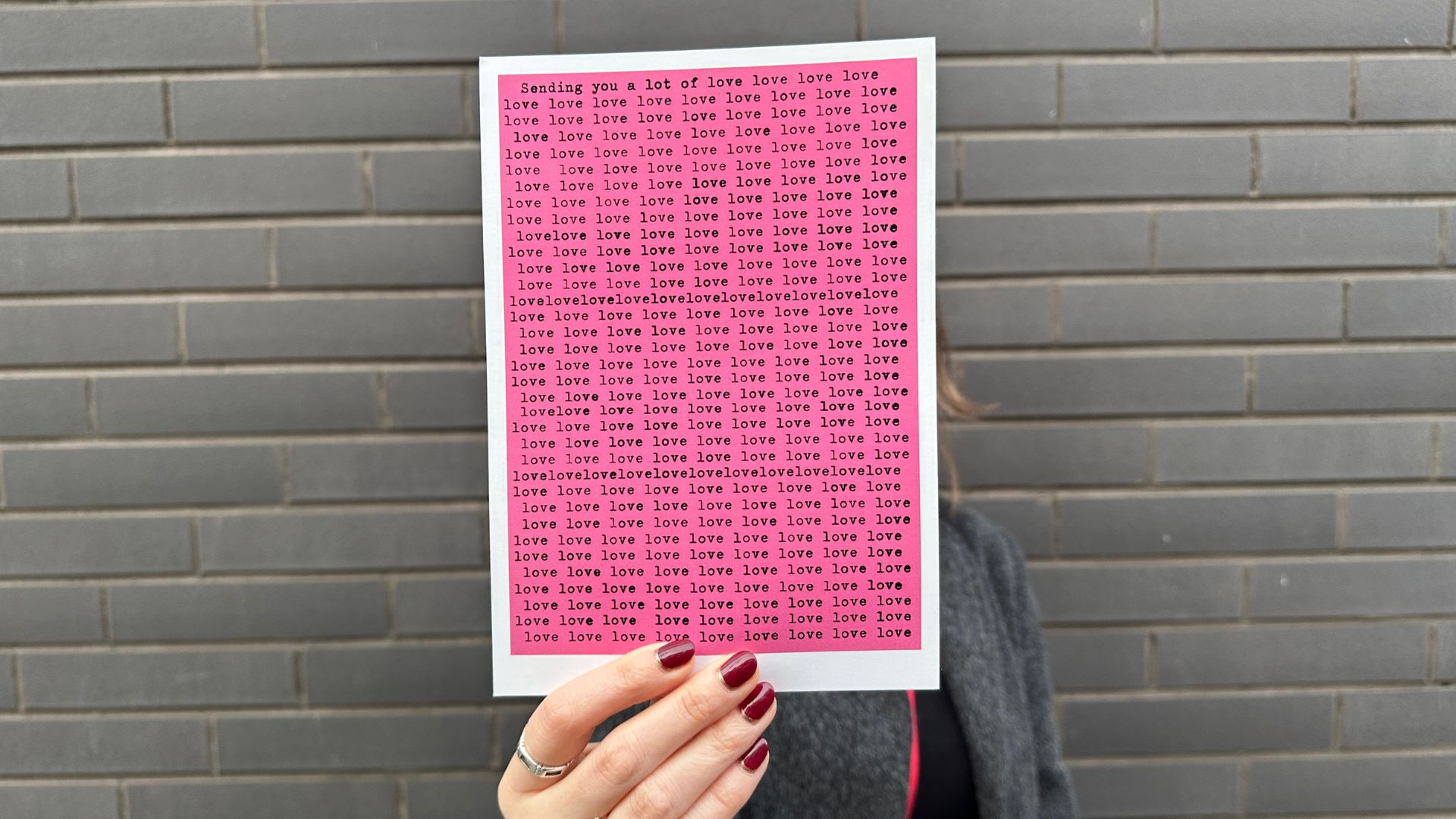 Grab a unique souvenir from the Moco store. © Visit London/Kirstine Spicer A person holding a pink postcard with the word love against a grey wall