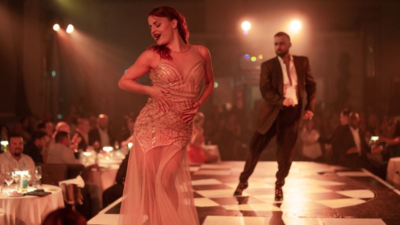 See dazzling performances, a live Latin band and flamboyant feathered costumes at The London Cabaret Club. Credit: The London Cabaret Club. Image courtesy of The London Cabaret Club. Woman in sequin dress dancing and singing on stage, with a man in black costume dancing behind her at the dimly lit London Cabaret Club.