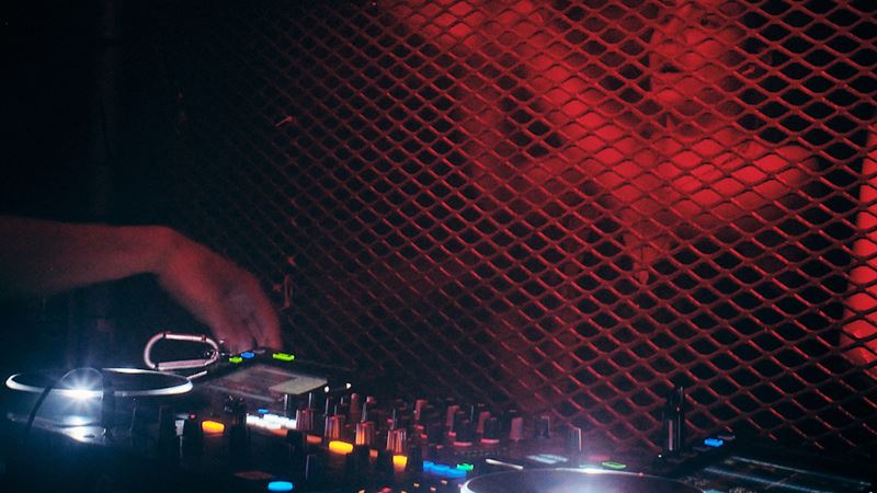 Head to this warehouse in South Bermondsey for house music and more. Credit: Louis Sartori. Image courtesy of Venue M.O.T Unit 18. Close-up of a DJ booth with woman dancing under red lighting in front of the booth.
