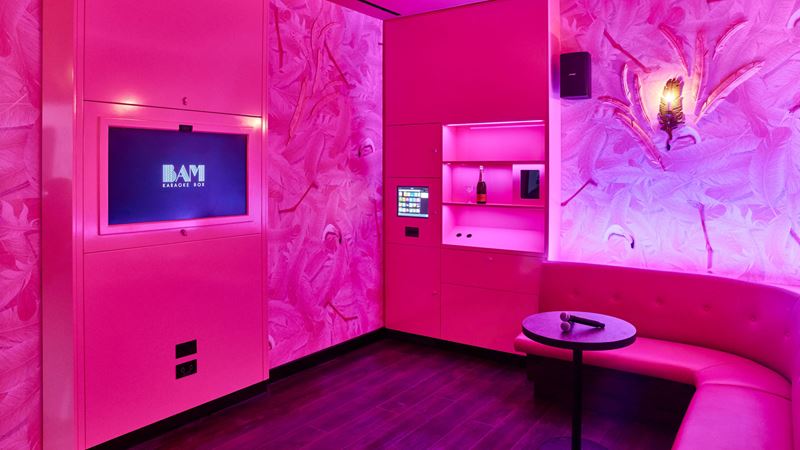Book one of the uniquely designed booths at BAM Karaoke Box. Credit: Sim Canetty-Clarke. Image courtesy of BAM Karaoke Box. A photo of a pink karaoke booth with two microphones on a table in front of the curved sofa, a TV on the wall and a bottle of prosecco on a shelf