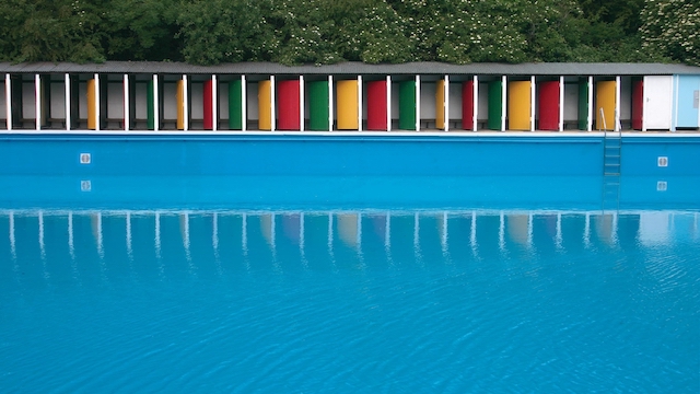Go for a swim at Tooting Bec Lido. ©Tooting Lido. Calm pool water and cabins with colourful doors at Tooting Bec Lido in south London.