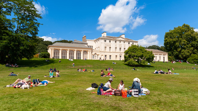 Enjoy the grounds and art of Kenwood House. Image courtesy of Shutterstock. Picnickers sit on the grass outside Kenwood House on Hampstead Heath on a sunny day.