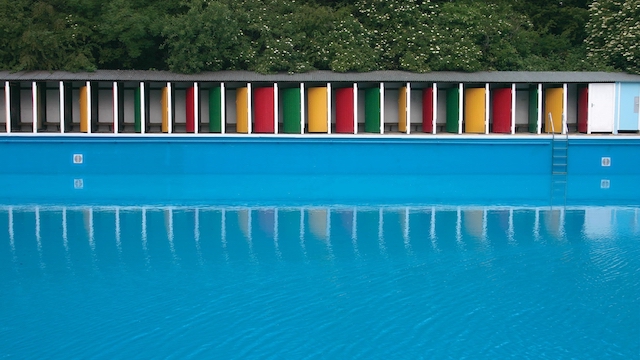Colourful doors looking out on the still water of the pool at Tooting Bec Lido in London.