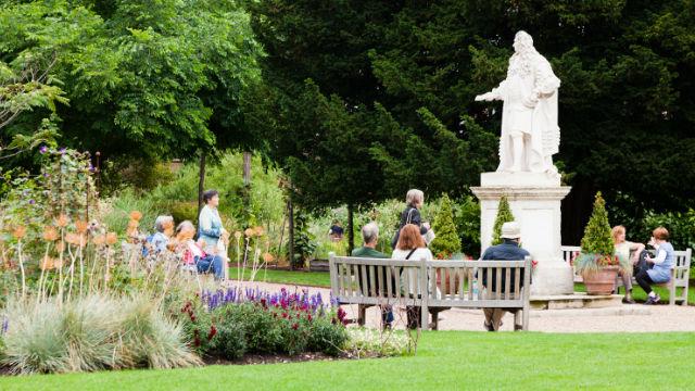 People sit on benches next to a statue in the chelsea physic garden.