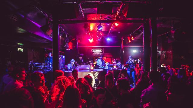 A music venue filled with people while a pianist is playing live music under pink, purple and blue spotlights.