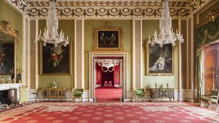 Landscape photo of the Green Drawing Room in Buckingham Palace; royal gold and red carpet, green panelled walls with large portraits hanging, high ceilings decorated in gold, green and gold furniture in the room
