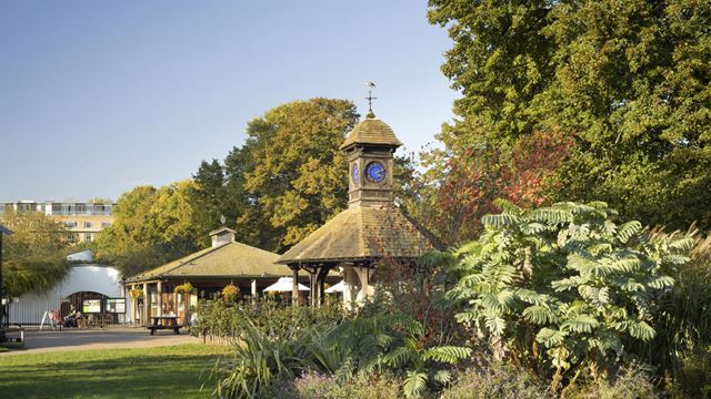 The entrance to the Diana, Princess of Wales Memorial Garden. There are leafy green trees in the foreground and a cafe further back.
