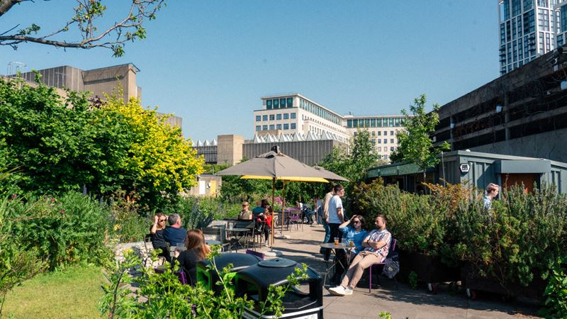 Relax in the sunshine at Queen Elizabeth Hall Roof Garden. Credit: Arnaud Mbaki. Image courtesy of Southbank Centre. People sitting and relaxing in the Queen Elizabeth Hall Roof Gardens on a sunny day.