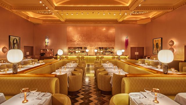 The yellow and gold interior of Sketch The Gallery restaurant showing the main seating area with the bar in the background.