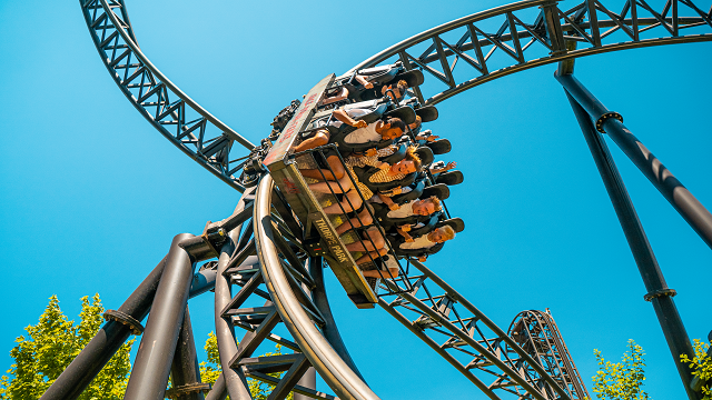 A rollercoaster on a high angled track, with people in the cart having fun in the sunshine