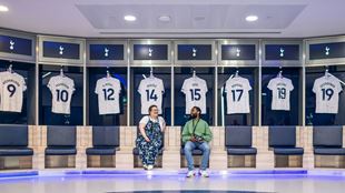 Two vistors are sitting in the changing rooms at the Tottenham Hotspur stadium and where the players' shirts are exhibited. 