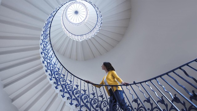 The Tulip Stairs at Queen's House, Greenwich. Image courtesy of Royal Museums Greenwich. A woman walking up the Tulip Stairs in the Queen's House, Greenwich.