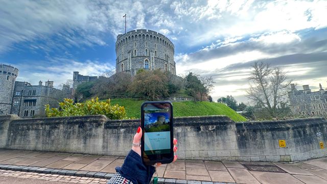 A hand holds up the auido guide at windsor castle against the walls. 