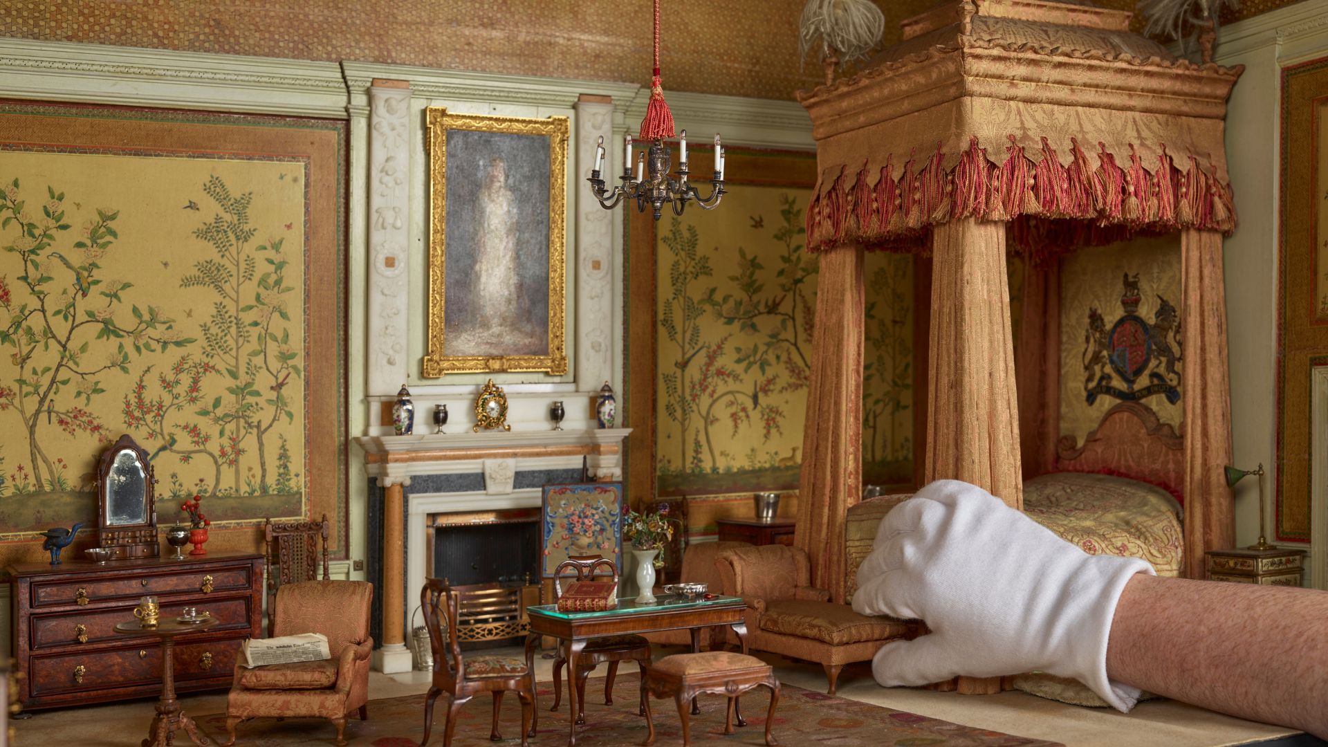 Be captivated by perfect replicas in the enchanting Queen Mary's Dolls' House. © Royal Collection Enterprises Limited 2025 | Royal Collection Trust A hand picks up furniture in the queen marys dolls house at windsor castle.